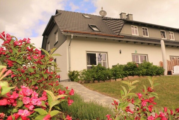 Een huis met twee verdiepingen, een schuin dak, een schoorsteen en een voordeur.