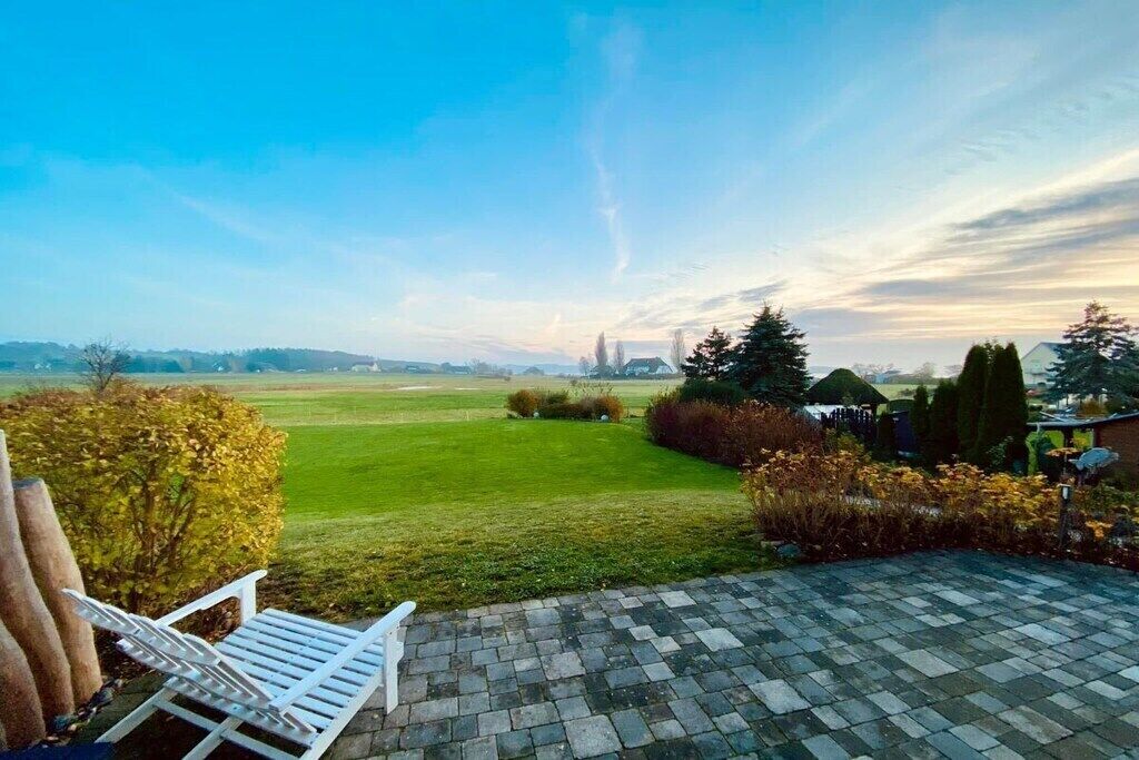 Eine Terrasse mit Blick auf eine Rasenfläche, ein weißer Stuhl und ein gepflasterter Bereich.