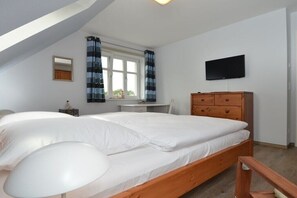 Ein Schlafzimmer mit einem Bett, einer Holzkommode, einem an der Wand befestigten Fernseher und einem Fenster mit Vorhängen.