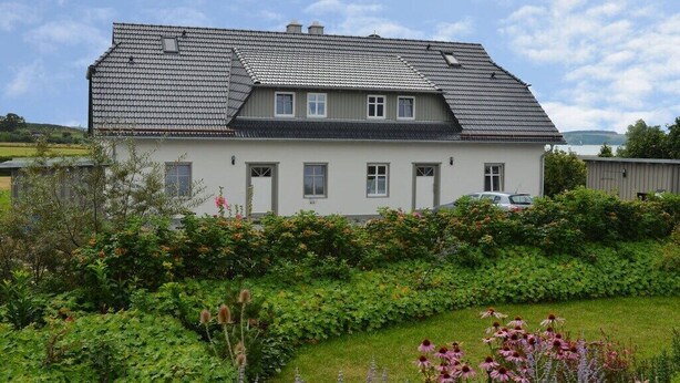 A two-story house with a sloped roof, a front garden with various plants, and a car parked in the driveway. - Feuerstein House Mönchgut (Mönchgut)