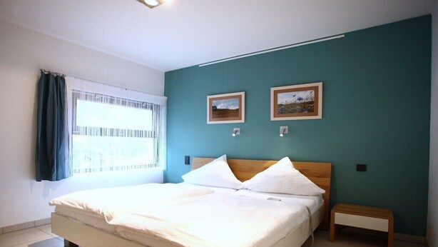 Une chambre à coucher avec un lit, une table de chevet, deux tableaux encadrés au mur et une fenêtre avec des rideaux.