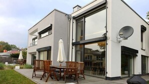 Une maison moderne à deux étages, dotée d’une terrasse, de mobilier d’extérieur et d’une antenne parabolique.