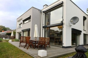 Ein modernes, zweistöckiges Haus mit Terrasse, Gartenmöbeln und einer Satellitenschüssel.