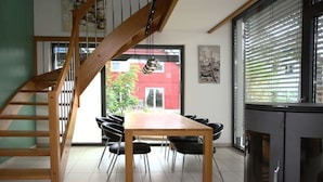 Un coin repas avec une table et des chaises en bois, un escalier et une vue sur un bâtiment rouge à l’extérieur.