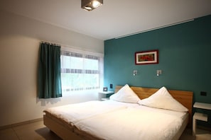 Ein Schlafzimmer mit Bett, Nachttisch, einem Fenster mit Vorhängen und einem an der Wand hängenden Bild.