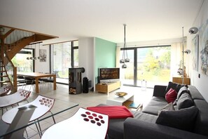 Ein modernes Wohnzimmer mit Treppe, Essbereich und großen Fenstern.