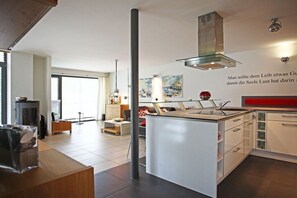 Eine moderne Küche mit Kochinsel, einer Edelstahl-Dunstabzugshaube und Blick auf den Wohnbereich.