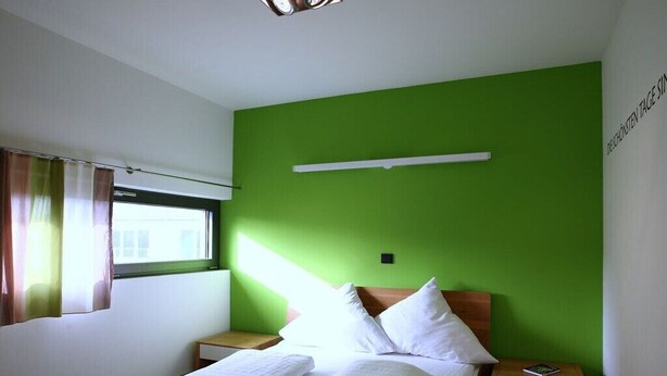 Une chambre d’hôtel avec un lit, deux tables de chevet, une fenêtre avec des rideaux et un mur vert.