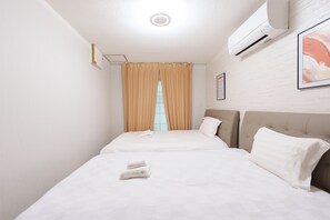 Ein Hotelzimmer mit zwei Betten, einem Fenster mit Vorhängen, einer Klimaanlage und einem gerahmten Bild an der Wand.