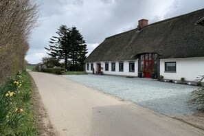 A traditional building with a thatched roof, a gravel driveway, and a row of windows. - Old Tenne under Reet in a single position (Taarstedt)