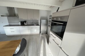 A modern kitchen with white cabinetry, a built-in oven, and a stainless steel range hood. - Old Tenne under Reet in a single position (Taarstedt)