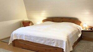 Uma cama de solteiro com cabeceira e peseira de madeira, duas luminárias de cabeceira e uma mesinha de cabeceira com abajur.