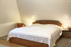 Ein Einzelbett mit Holz-Kopf- und Fußteil, zwei Nachttischlampen und ein kleiner Nachttisch mit Lampe.