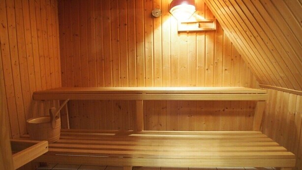 A wooden sauna with benches and a wall-mounted heater. - Holiday home Ockholm (Ockholm)