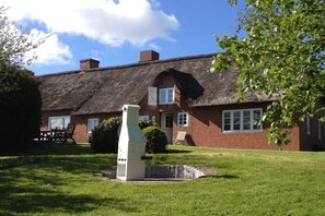 Een huis met rieten dak, een witte schoorsteen, een gazon en een boom.