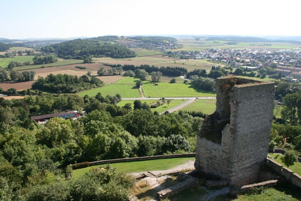 Ein historischer Stein-Turm mit einer umlaufenden Grünfläche und einem Dorf in der Ferne.