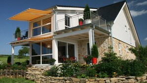 Ein zweigeschossiges Haus mit Balkon, Stein Fundament und einem Garten mit verschiedenen Pflanzen.