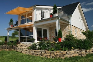 A two-story house with a balcony, stone foundation, and a garden with various plants. - Holiday home Hörnchens Hörle (Volkmarsen-Hörle)