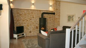 Ein Wohnzimmer mit Steinswand, Kamin, Sofa, Fernseher und einer Treppe.