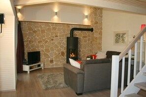 A living room with a stone wall, a fireplace, a sofa, a TV, and a staircase. - Holiday home Hörnchens Hörle (Volkmarsen-Hörle)