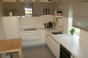 Een moderne keuken met witte kasten, een roestvrijstalen afzuigkap, een koffiezetapparaat en een klein raam met een plant.