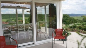 Eine verglaste Terrasse mit Gartenmöbeln, einem roten Sessel und Blick auf eine grüne Landschaft.