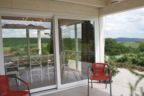 Eine verglaste Terrasse mit Gartenmöbeln, einem roten Sessel und Blick auf eine grüne Landschaft.