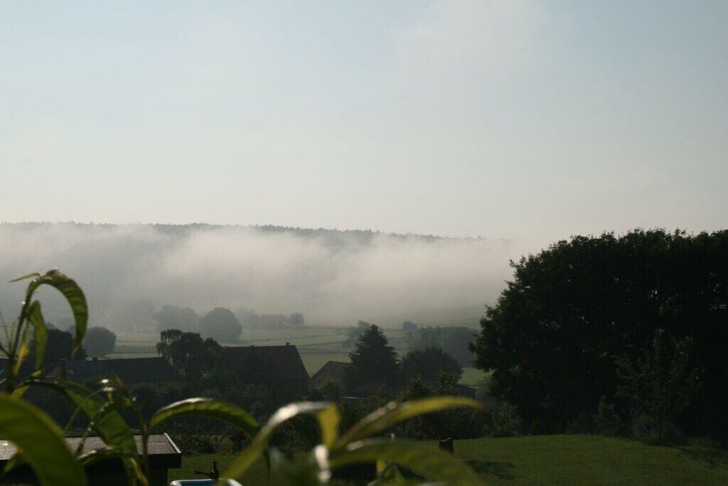 A rural landscape with a foggy horizon, greenery, and a few buildings.