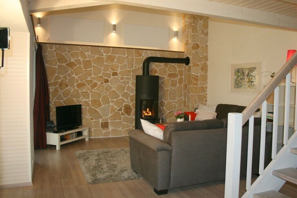 A living room with a stone wall, a fireplace, a sofa, a TV, and a staircase.