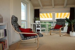 Ein Zimmer mit zwei gemusterten Stühlen, einem kleinen Tisch und einem Bücherregal.