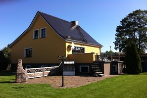 Ein zweigeschossiges gelbes Haus mit dunklem Dach, Steinsschornstein und gepflasterter Auffahrt.