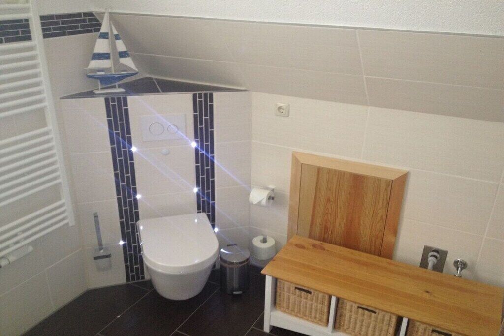 Un baño con inodoro blanco, tocador de madera y un pequeño cubo de basura.