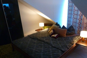 Ein Schlafzimmer mit Bett, Kissen, einem Nachttisch mit Lampe und einer Wand mit Muster.