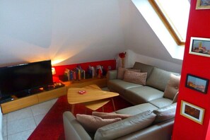 Ein Wohnzimmer mit Flachbildfernseher, einer Couch, einem Couchtisch und einem Bücherregal.