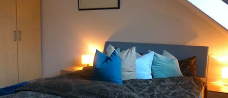 A bedroom with a bed, pillows, a nightstand, and a framed picture on the wall.