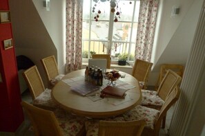 A round dining table with six chairs, a window with curtains, and a view of the outside. - Holiday apartment Wedel (Augsburg)