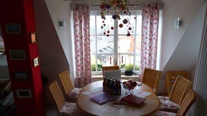 Un comedor con una mesa redonda, sillas con estampado floral y vistas al exterior a través de una ventana con cortinas.