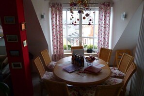A dining area with a round table, floral chairs, and a view of the outside through a window with curtains.