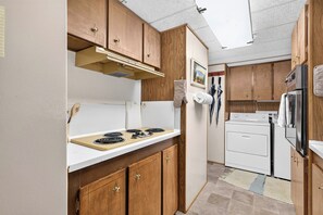 Une cuisine de taille réduite, dotée de meubles en bois, d’une cuisinière, d’un réfrigérateur et d’un lave-linge.
