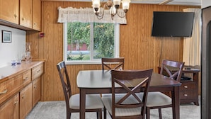 Kompakti keittiö, jossa on puiset kaapit, ruokapöytä neljällä tuolilla, seinälle asennettu televisio ja ikkuna, josta avautuu näkymä vehreään maisemaan.