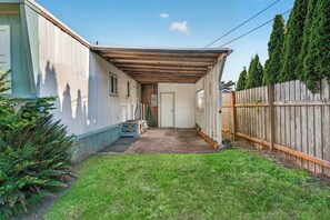 Un petit jardin à l’arrière de la maison, avec une terrasse en bois, une petite pelouse et une clôture en bois.