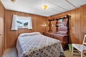 A bedroom with a wooden paneled wall, a bed with patterned bedding, a dresser with a mirror, and a window with curtains. - Close to Beach & Dtwn! Extended Long Beach Stay (Long Beach)