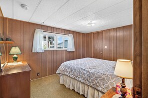Une chambre à coucher avec un lit, une fenêtre avec des rideaux, une lampe de chevet et un panneau mural en bois.