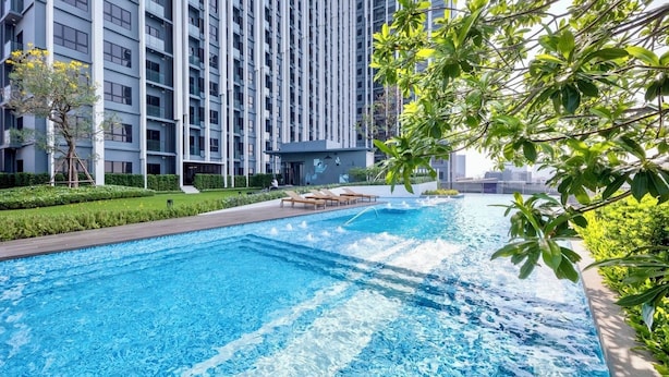 A swimming pool with clear blue water, surrounded by a landscaped garden and a modern building with balconies. - Top-Floor Condo Next to MRT Blue Line, Near Malls, Pool, Gym & Quiet Living (Krung Thep Maha Nakhon)