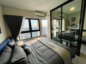 A modern hotel room with a large bed, a view of the city, and a sliding glass door leading to a balcony. - Top-Floor Condo Next to MRT Blue Line, Near Malls, Pool, Gym & Quiet Living (Krung Thep Maha Nakhon)