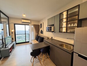A modern kitchen with a dining area, a large window with a city view, and a built-in microwave. - Top-Floor Condo Next to MRT Blue Line, Near Malls, Pool, Gym & Quiet Living (Krung Thep Maha Nakhon)