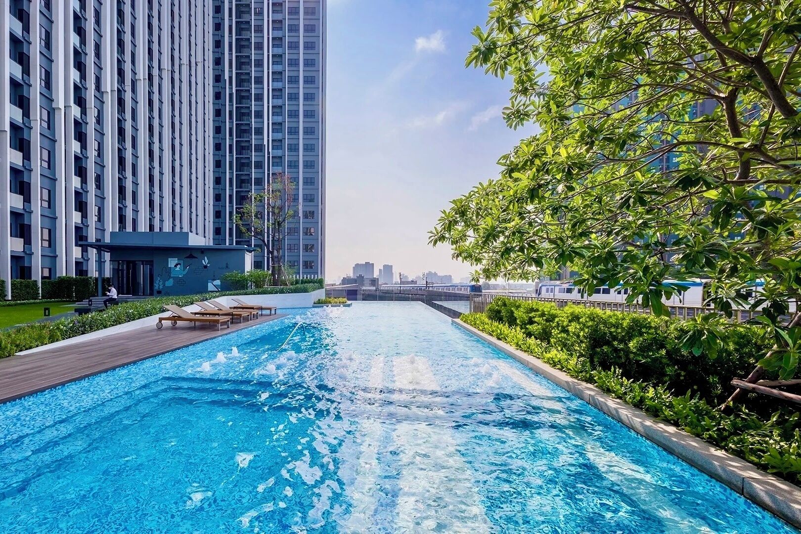 Piscina con vistas a un horizonte urbano, rodeada de vegetación y edificios modernos.