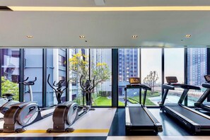 A gym with cardio equipment, a treadmill, and a stationary bike, with a view of buildings and greenery. - Top-Floor Condo Next to MRT Blue Line, Near Malls, Pool, Gym & Quiet Living (Krung Thep Maha Nakhon)