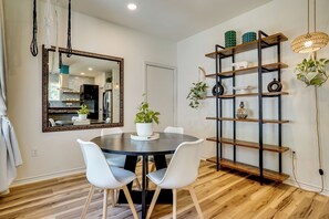 Un coin repas avec une table ronde, des chaises blanches, un miroir et une bibliothèque en bois agrémentée d’objets décoratifs.