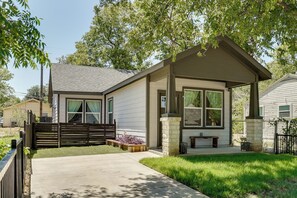 A small, single-story house with a front porch, a wooden deck, and a stone pillar. - Historic Southside Fort Worth Home w/ Fenced Yard! (Fort Worth)